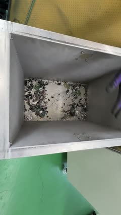 A metal bin containing scattered metal scraps and debris, viewed from above as if captured in a short mp4 video. The floor is green and a yellow surface is visible in the background.